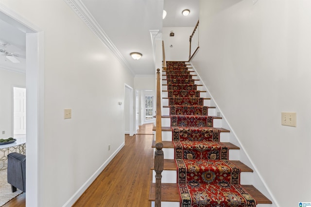 stairway with ceiling fan, crown molding, baseboards, and wood finished floors