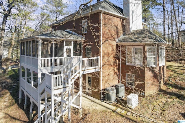 exterior space featuring a sunroom, a chimney, stairway, central air condition unit, and brick siding