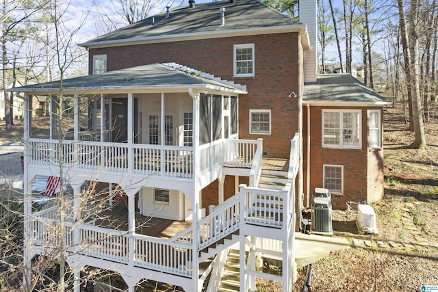 back of house with a sunroom, a chimney, stairway, and brick siding