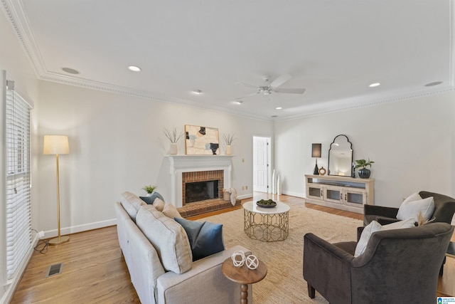 living room with a brick fireplace, wood finished floors, visible vents, and crown molding