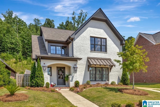 view of front of property featuring brick siding, a front lawn, a shingled roof, and fence