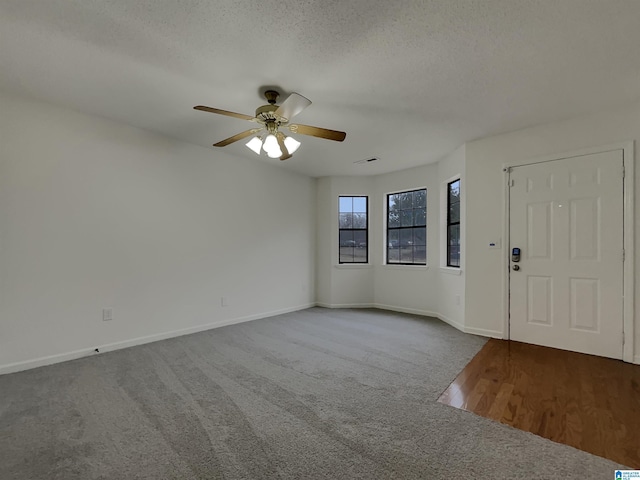 carpeted entrance foyer featuring a ceiling fan, visible vents, baseboards, and a textured ceiling