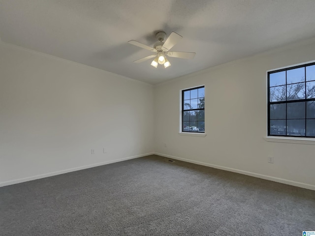 empty room featuring crown molding, dark colored carpet, visible vents, a ceiling fan, and baseboards