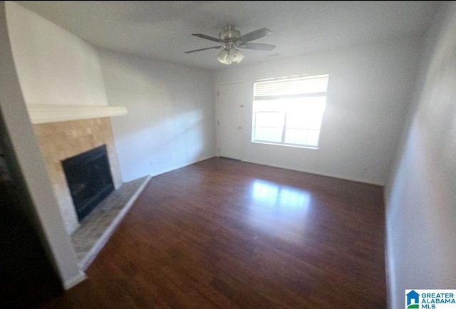 unfurnished living room with dark wood-style flooring, a tiled fireplace, and a ceiling fan