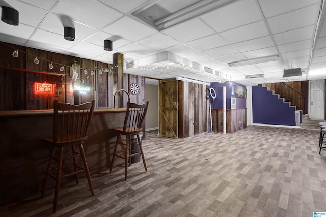 bar with stairs, a bar, wood walls, and a paneled ceiling