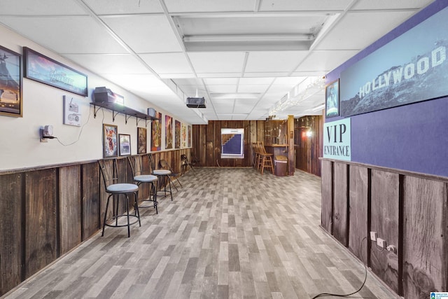 interior space featuring light wood finished floors, wooden walls, a bar, a wainscoted wall, and a paneled ceiling