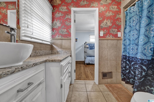 ensuite bathroom with connected bathroom, a wainscoted wall, vanity, tile walls, and wallpapered walls