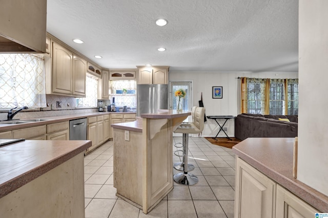 kitchen with a breakfast bar, stainless steel appliances, light brown cabinetry, open floor plan, and light tile patterned flooring