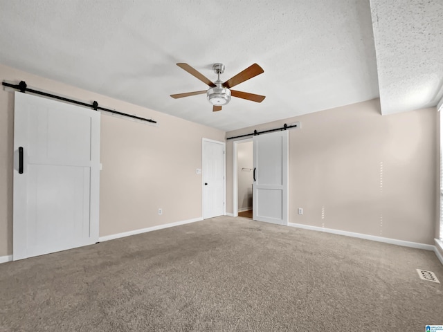 unfurnished bedroom with a textured ceiling, carpet floors, a barn door, and visible vents