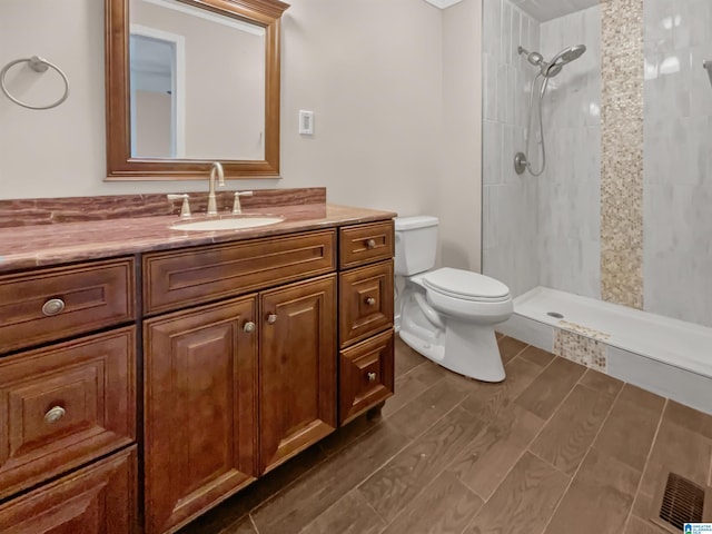 bathroom featuring toilet, a tile shower, wood finished floors, and vanity