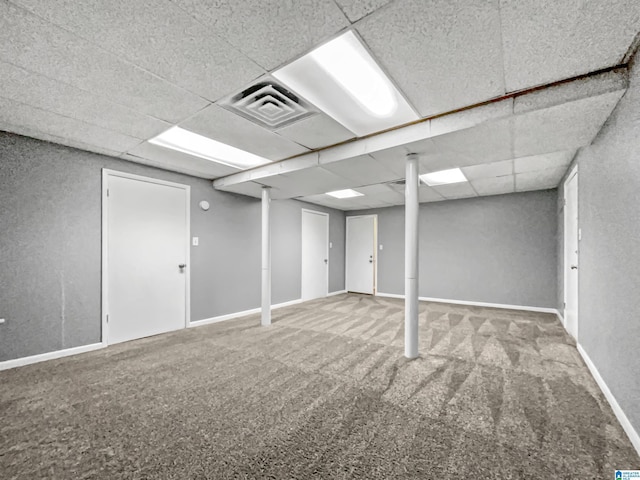 finished below grade area featuring a drop ceiling, carpet, visible vents, and baseboards