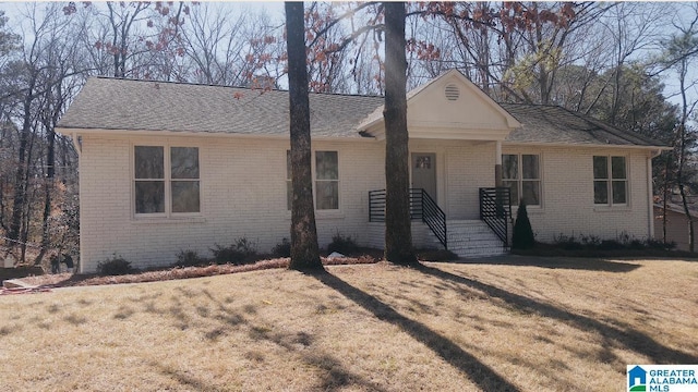 view of front of property featuring brick siding, a front lawn, and roof with shingles