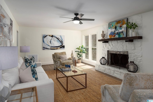 living room with ceiling fan, visible vents, wood finished floors, and a stone fireplace