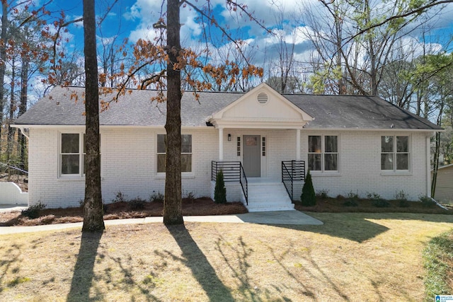 view of front facade with covered porch, roof with shingles, a front lawn, and brick siding