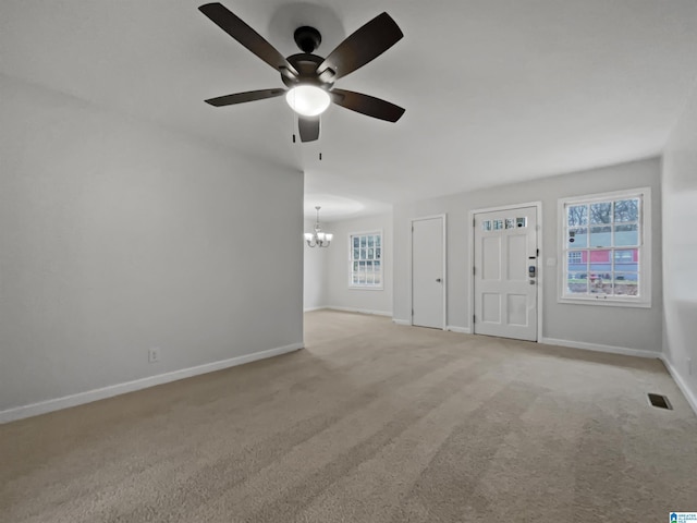 unfurnished living room featuring light carpet, ceiling fan with notable chandelier, a wealth of natural light, and baseboards