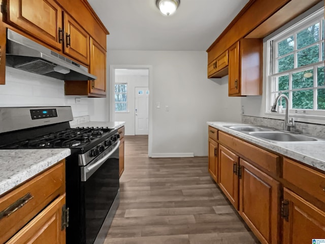 kitchen featuring gas range, under cabinet range hood, brown cabinetry, and a sink