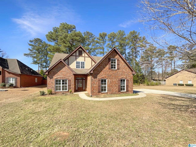 english style home featuring a shingled roof, a front yard, brick siding, and stucco siding