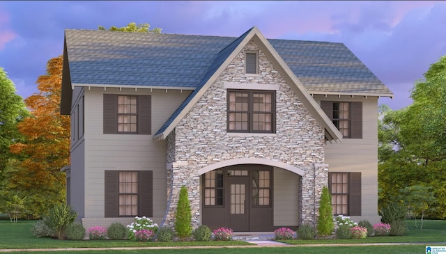 view of front of property featuring stone siding, a shingled roof, and a yard