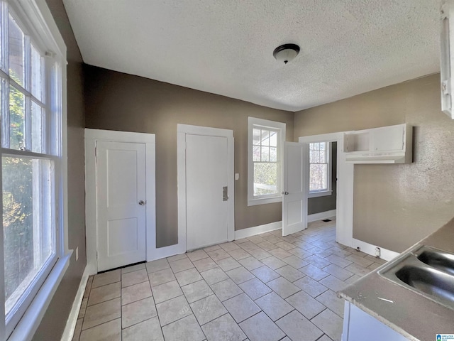 interior space with light tile patterned floors, light countertops, white cabinets, a sink, and a textured ceiling