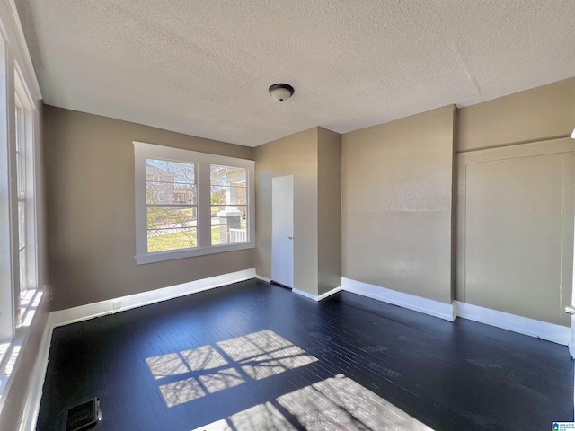 empty room featuring visible vents, a textured ceiling, baseboards, and dark wood-type flooring