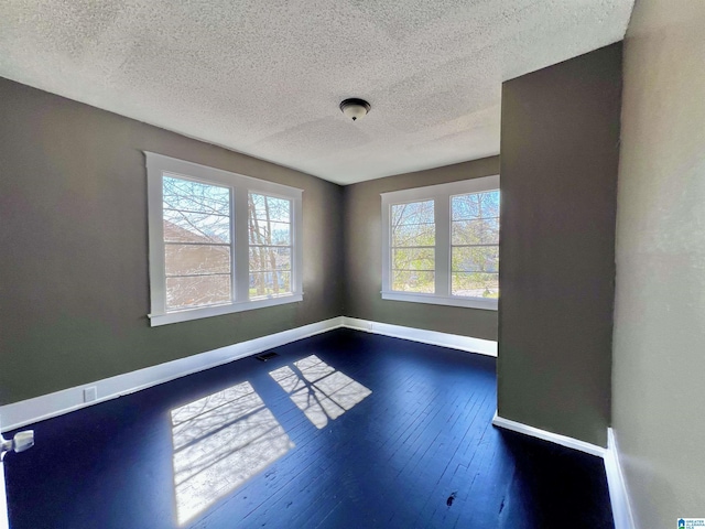 unfurnished room with visible vents, dark wood finished floors, a textured ceiling, and baseboards