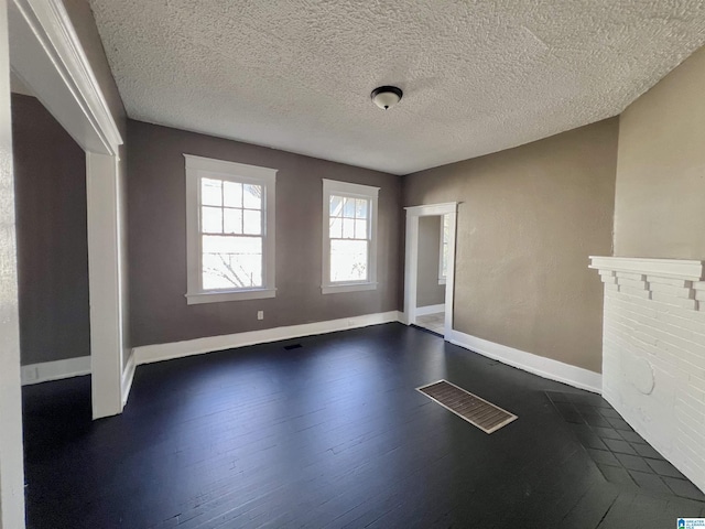 spare room with dark wood-style floors, a textured ceiling, visible vents, and baseboards