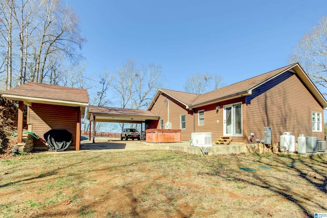 rear view of house with a carport, driveway, a hot tub, and a lawn