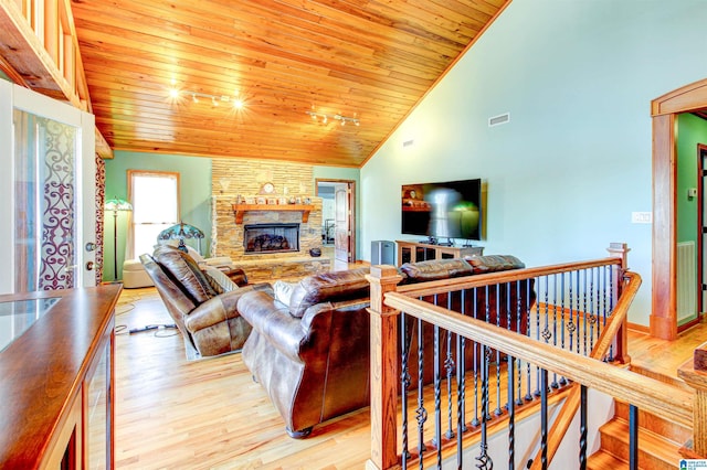 living area featuring light wood finished floors, wood ceiling, visible vents, and a stone fireplace