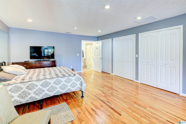 bedroom with two closets, recessed lighting, light wood-style floors, a textured ceiling, and baseboards