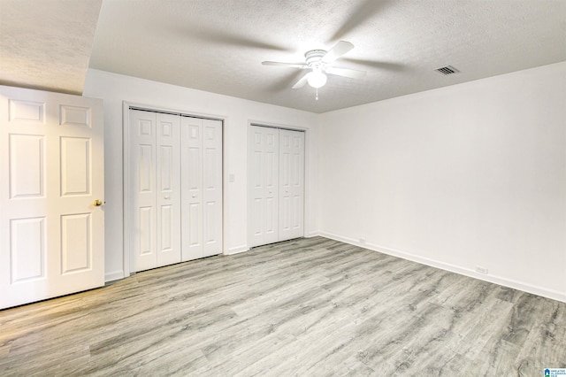 unfurnished bedroom with multiple closets, light wood-style flooring, a ceiling fan, a textured ceiling, and baseboards