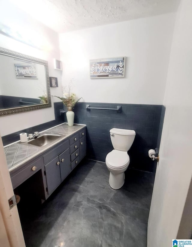 1525 NW Ridge St, Cullman, AL 35055 - half bathroom with a wainscoted wall, toilet, vanity, a textured ceiling, and tile walls