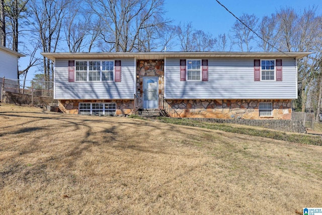 raised ranch featuring stone siding, fence, and a front lawn