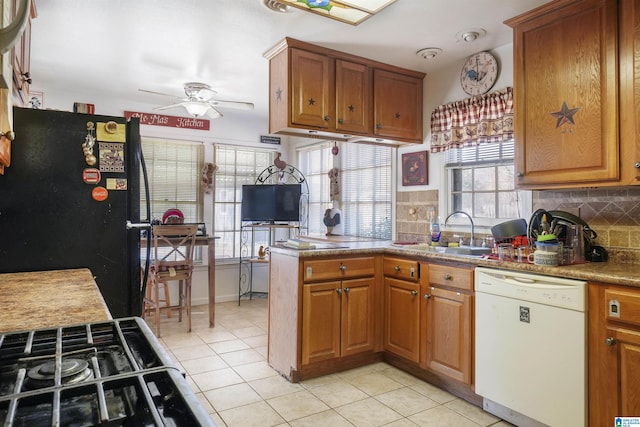 kitchen featuring tasteful backsplash, brown cabinetry, freestanding refrigerator, white dishwasher, and a sink