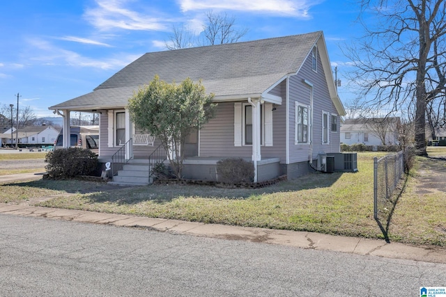 bungalow-style home with fence, a front lawn, cooling unit, and roof with shingles