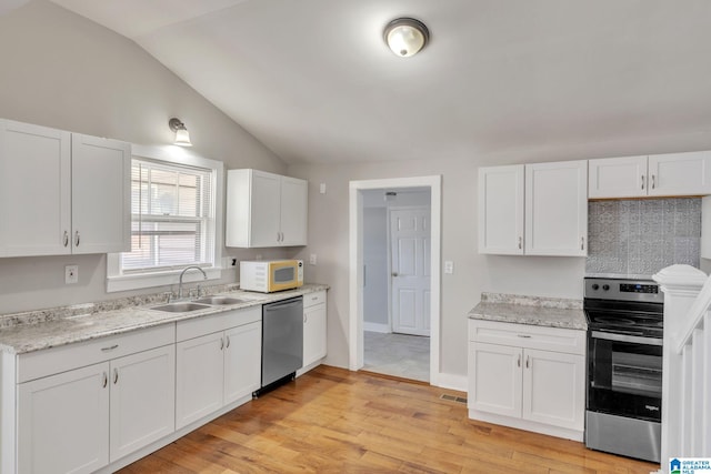 kitchen with stainless steel appliances, vaulted ceiling, white cabinets, and a sink