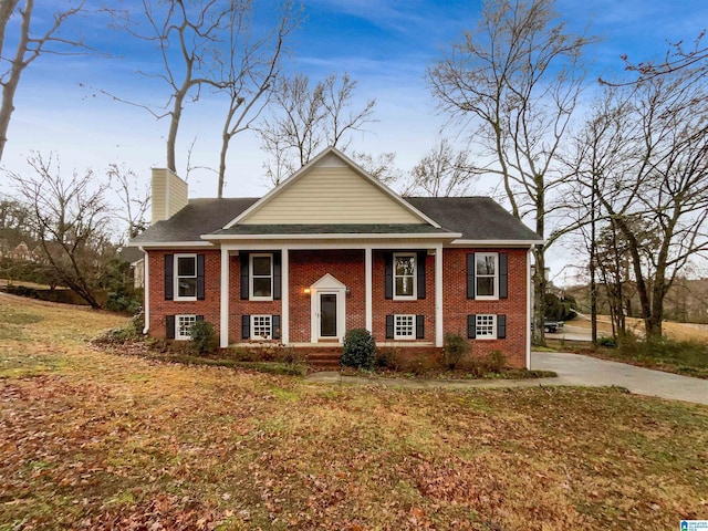 view of front of home with brick siding, a chimney, and a front lawn