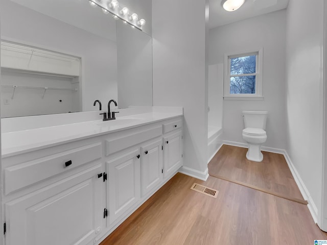 bathroom featuring toilet, wood finished floors, vanity, visible vents, and baseboards