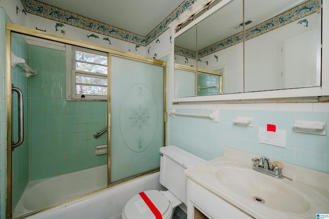 bathroom featuring tile walls, visible vents, toilet, combined bath / shower with glass door, and vanity