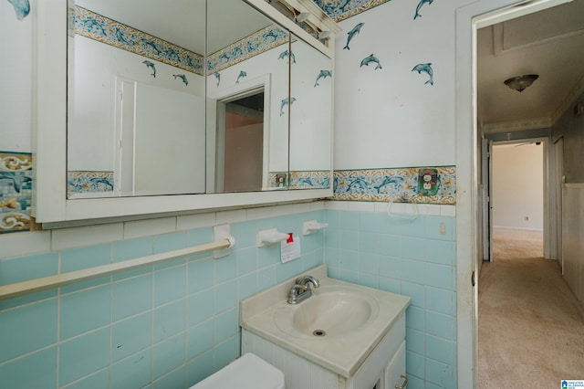 half bathroom featuring a wainscoted wall, tile walls, wallpapered walls, and vanity