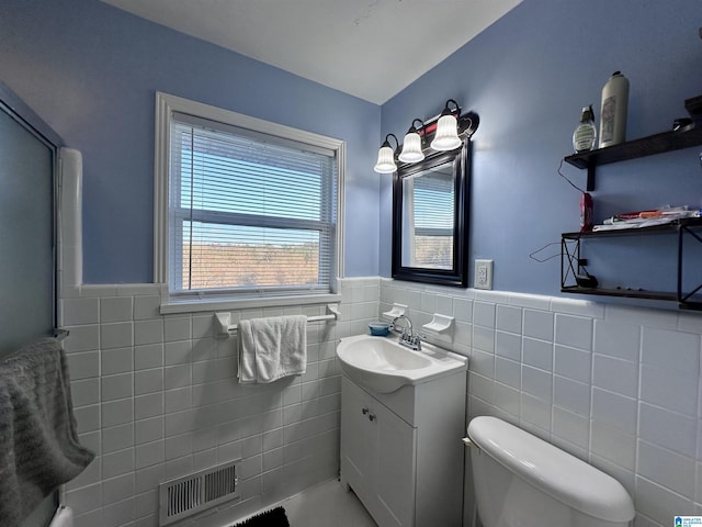 bathroom featuring vanity, toilet, visible vents, wainscoting, and tile walls