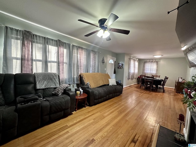 living area featuring baseboards, hardwood / wood-style floors, and a ceiling fan