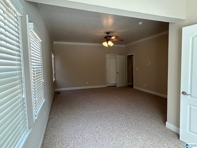 unfurnished room with light colored carpet, ornamental molding, ceiling fan, a textured ceiling, and baseboards