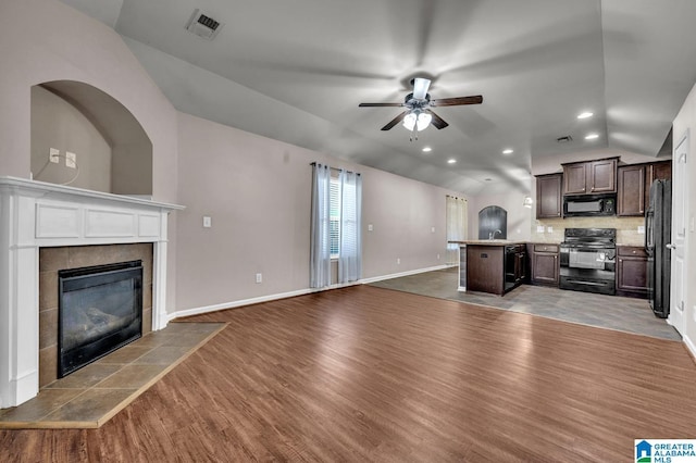 unfurnished living room with visible vents, ceiling fan, vaulted ceiling, wood finished floors, and a tile fireplace