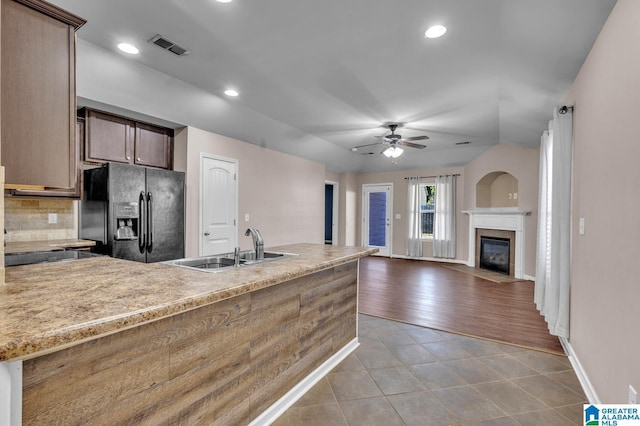 kitchen featuring black fridge with ice dispenser, a fireplace with flush hearth, a sink, a peninsula, and tile patterned floors