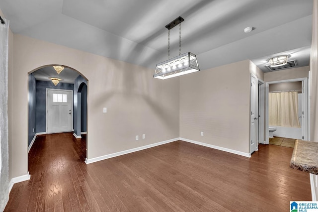 unfurnished dining area featuring arched walkways, dark wood-style flooring, vaulted ceiling, and baseboards