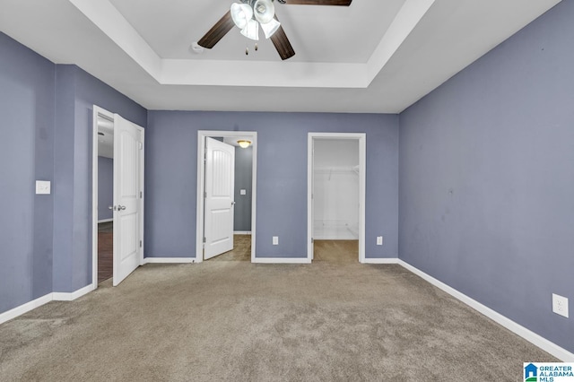 unfurnished bedroom with carpet floors, a spacious closet, baseboards, and a raised ceiling