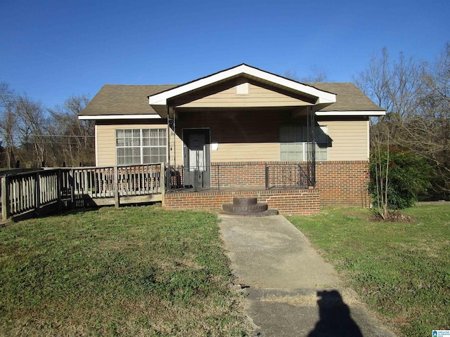 view of front of house featuring a front yard, brick siding, a deck, and roof with shingles