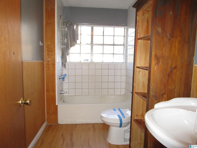 bathroom featuring shower / bathtub combination, toilet, wood walls, wood finished floors, and a sink