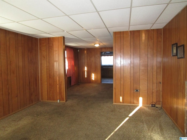 hall featuring carpet, a paneled ceiling, wooden walls, and baseboards