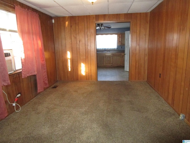 empty room with ceiling fan, cooling unit, a paneled ceiling, wood walls, and dark colored carpet